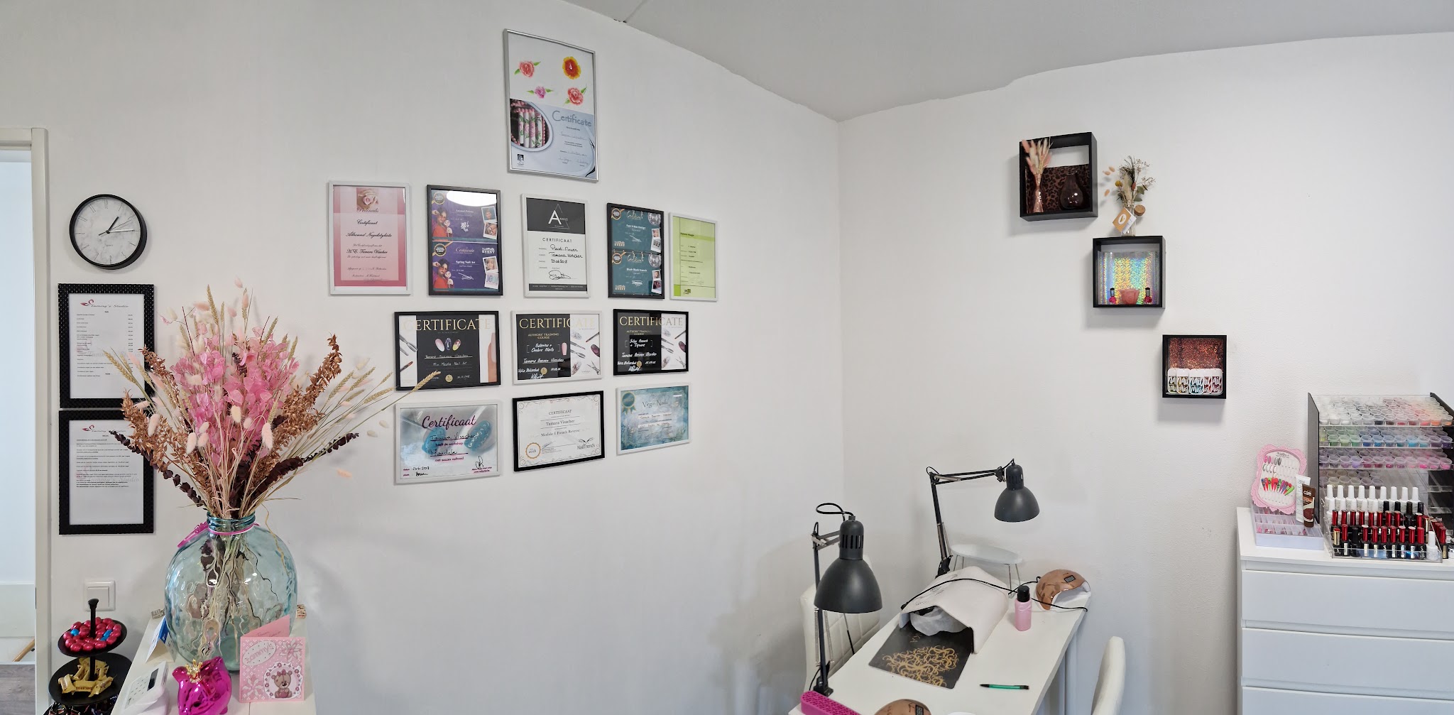 De studio met de certificatenmuur, bloemen en de werktafel met lamp