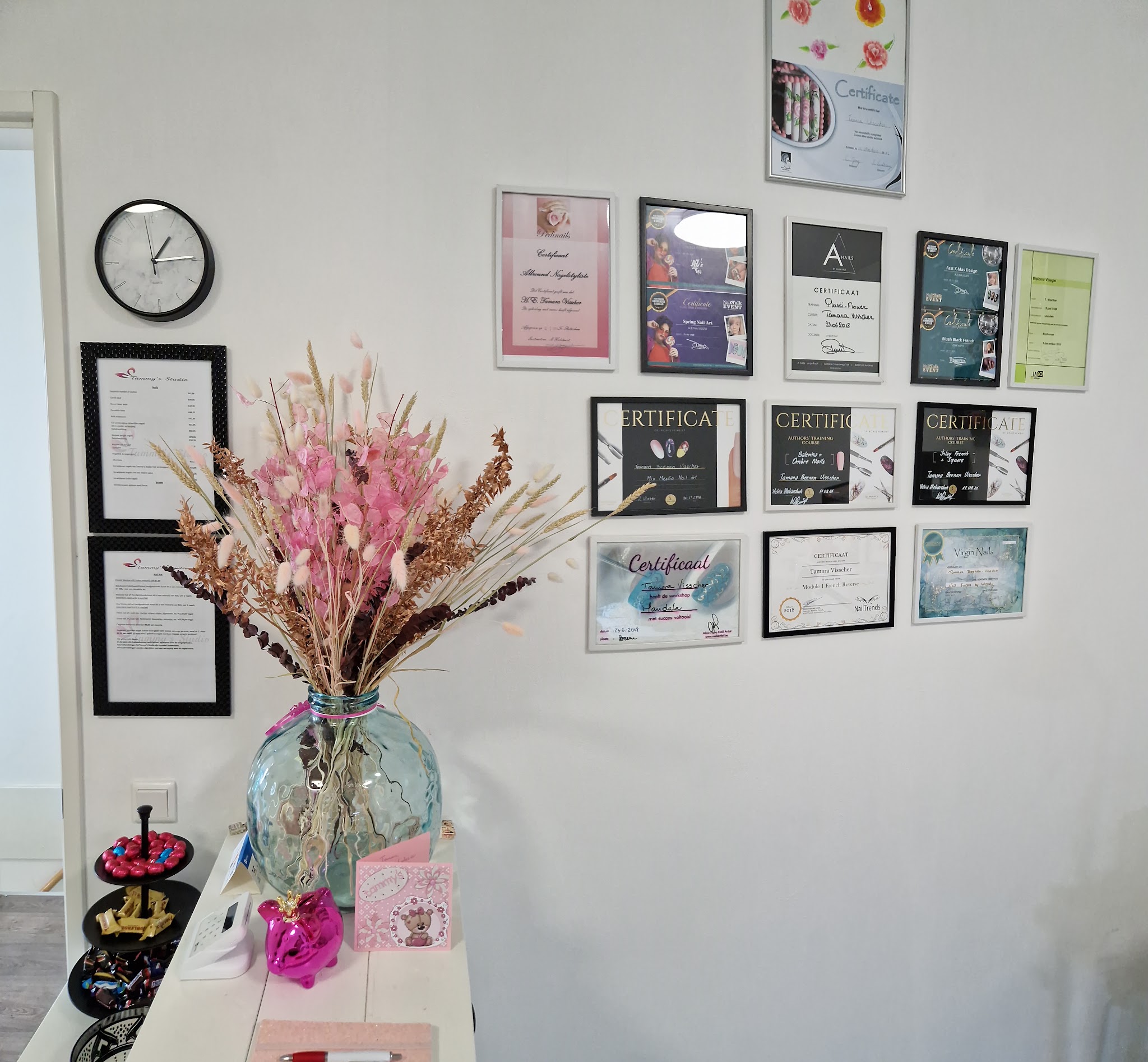 Muur met ingelijste certificaten en een vaas met roze droogbloemen